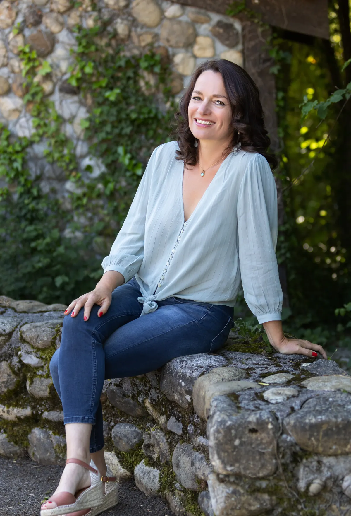 Gaëlle Yeretzian, souriante, assise sur un muret de pierre dans un jardin